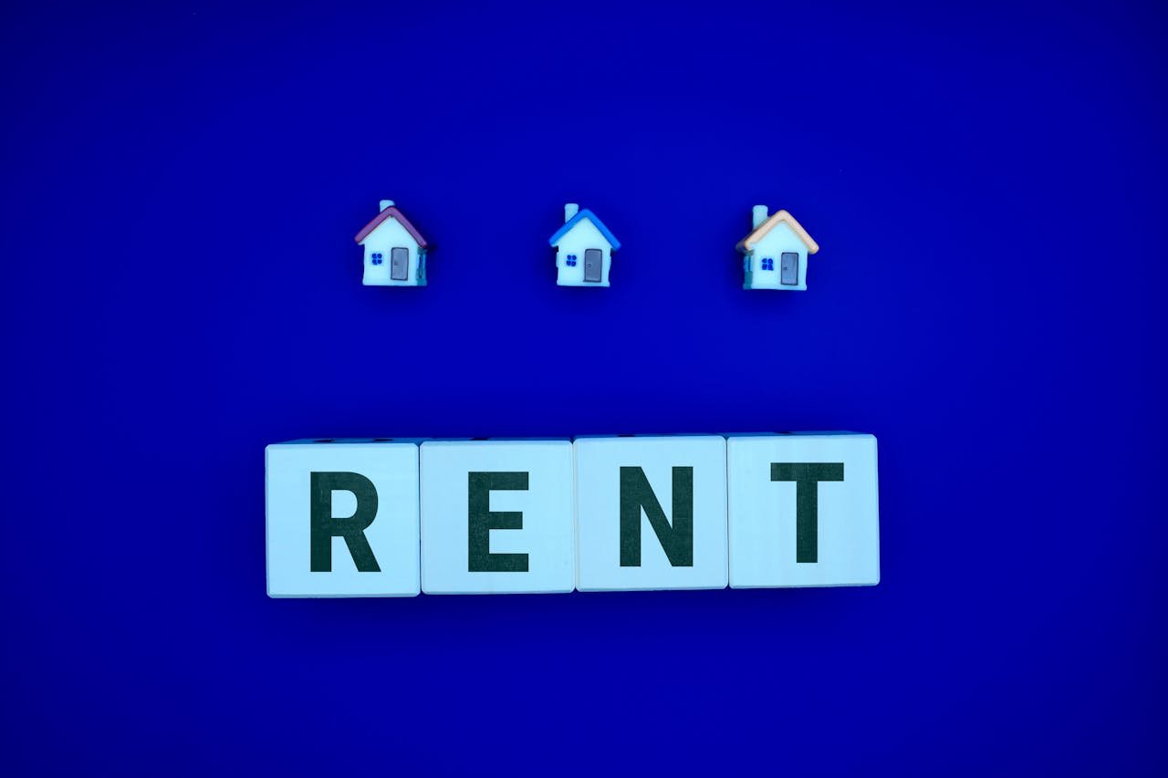 Miniature houses above letters spelling 'RENT' on a blue background, ideal for real estate themes.