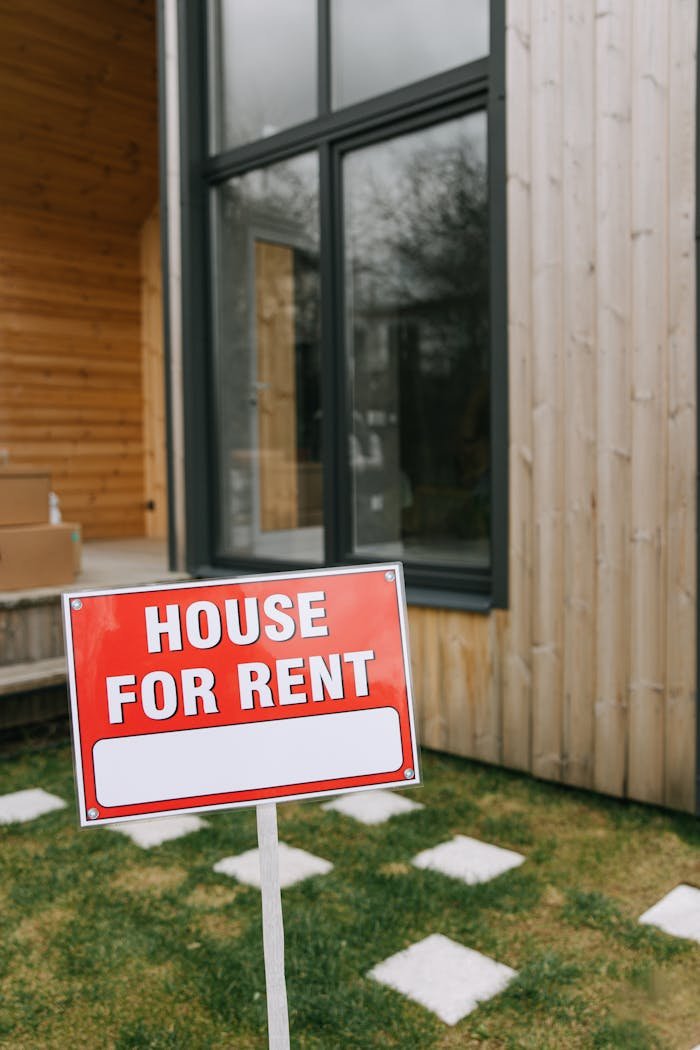 A modern wooden house with a bold 'House for Rent' sign on a grassy lawn, showcasing rental opportunity.